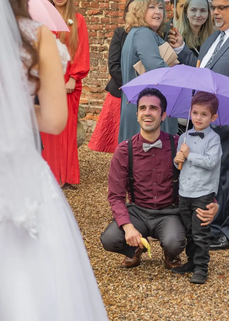 Young wedding guest with his dad and a lilac umbrella admire the bride at Leez Priory