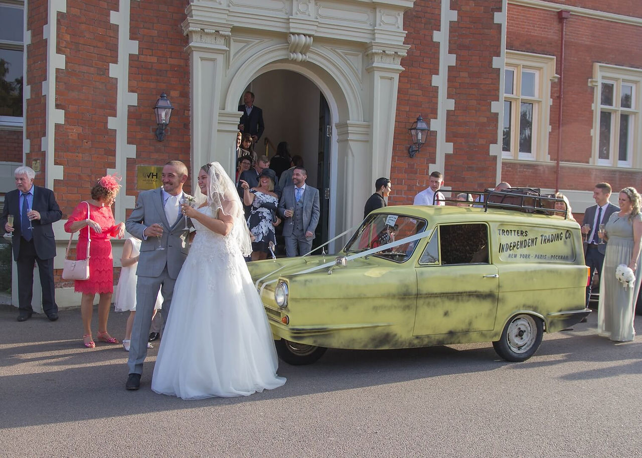Bride and groom standing in front pf a yellow Only Fools & Horses Reliant Robin van outside the front entrance pf Wivenhoe House Hotel