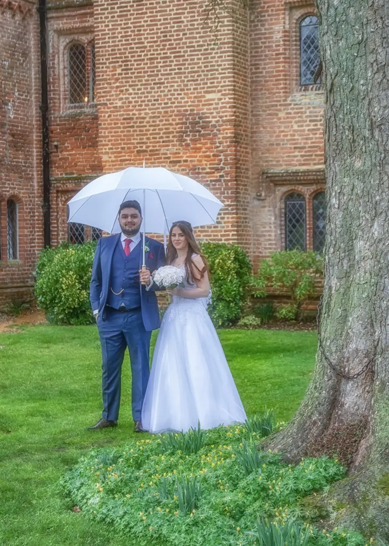 Bride and groom in the rain at Leez priory with a white wedding umbrella