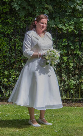 Bride in white tea length dress with jacket and white bouquet