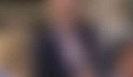 Groom in pink shirt and navy blazer talks to wedding guests at Great Lodge