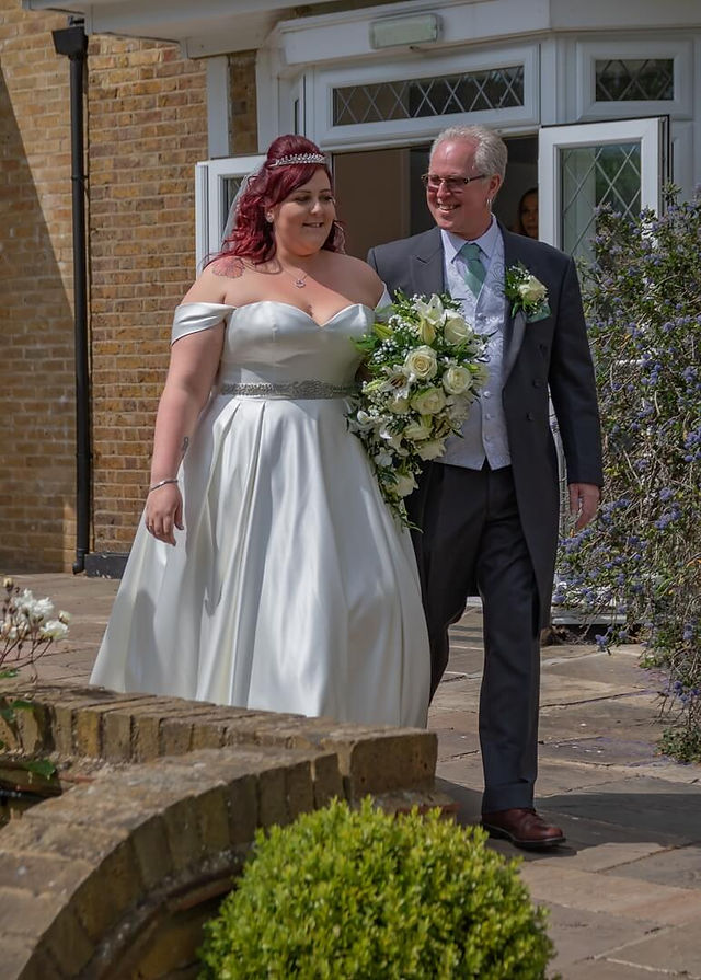 Bride enters outdoor ceremony on fathers arm with a large teardrop bouquet of cream roses