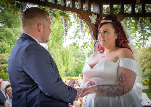 Bride and groom gaze at each other as they exchange vows and rings in an outdoor ceremony