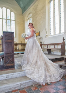 Bride looks over her shoulder as she stands on the steps inside the church at Great Waldingfield to show off her train