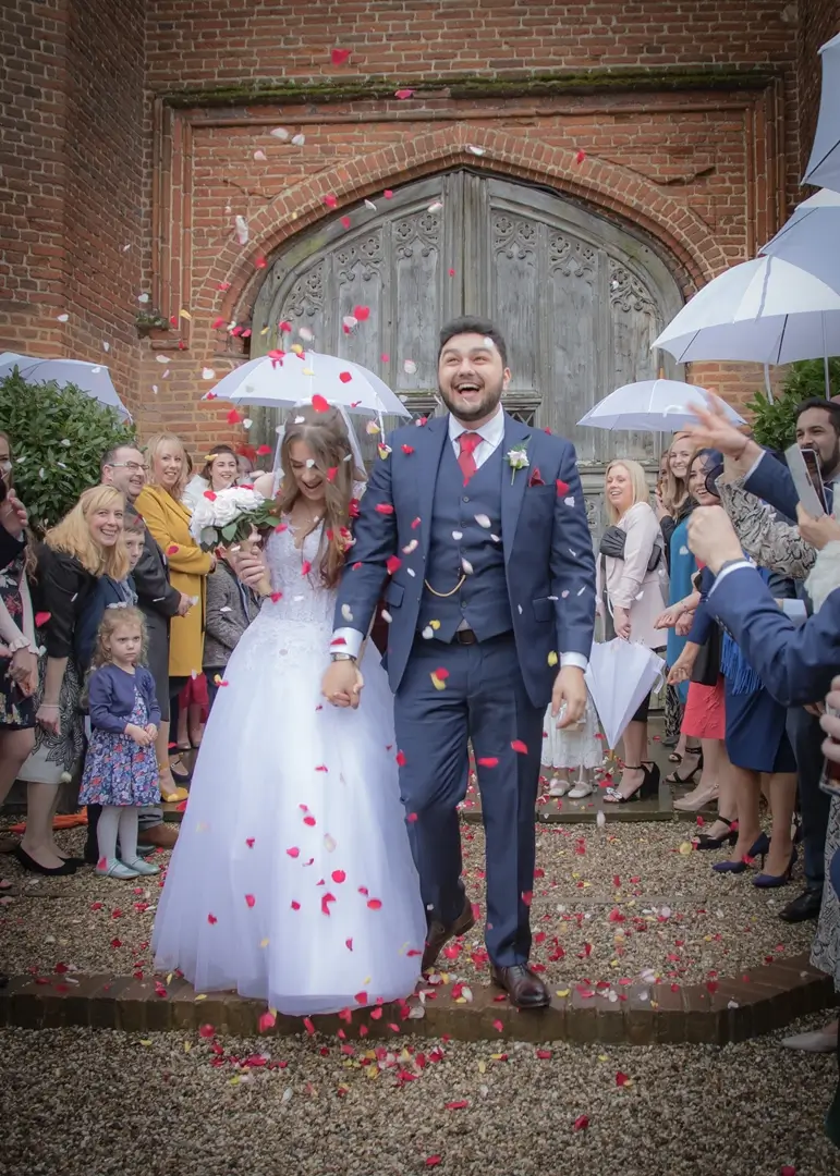 Bride and groom react to wedding confetti on a rainy day at Leez Priory