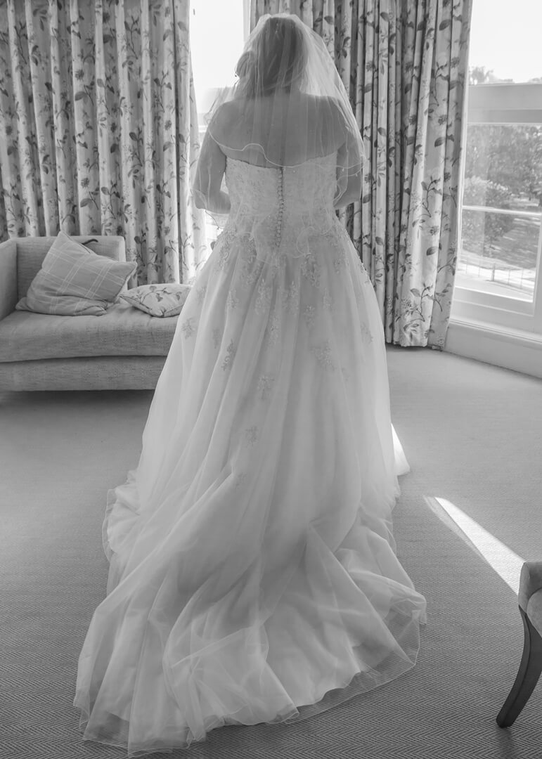 Black and white view of bride from behind as she looks out of the windows