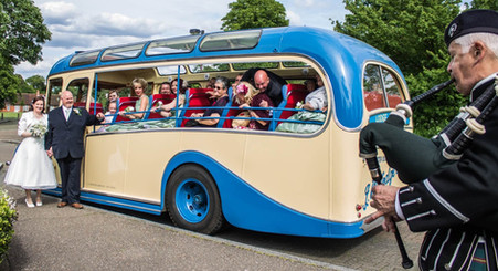 Bride and groom stand by their vintage coach wedding transport as a Scottish piper serenades them and their guests