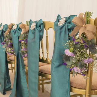 Row of chairs with green sating ribbons and hessian tied scottish flowers in purples ready for the wedding ceremony at Prested Hall