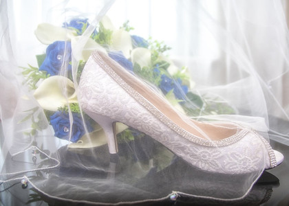 White wedding shoes and cream and blue bouquet with the brides veil laying over them