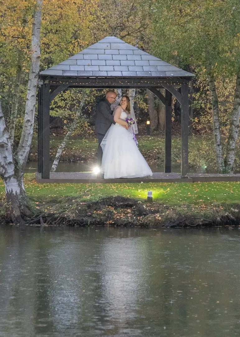Bride and groom shelter under the pergola as the rain comes down around them