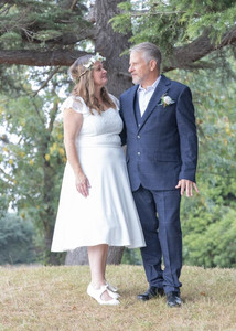 Bride in a tea length dress and groom in a dark blue suit  gaze at each other in front of a tree