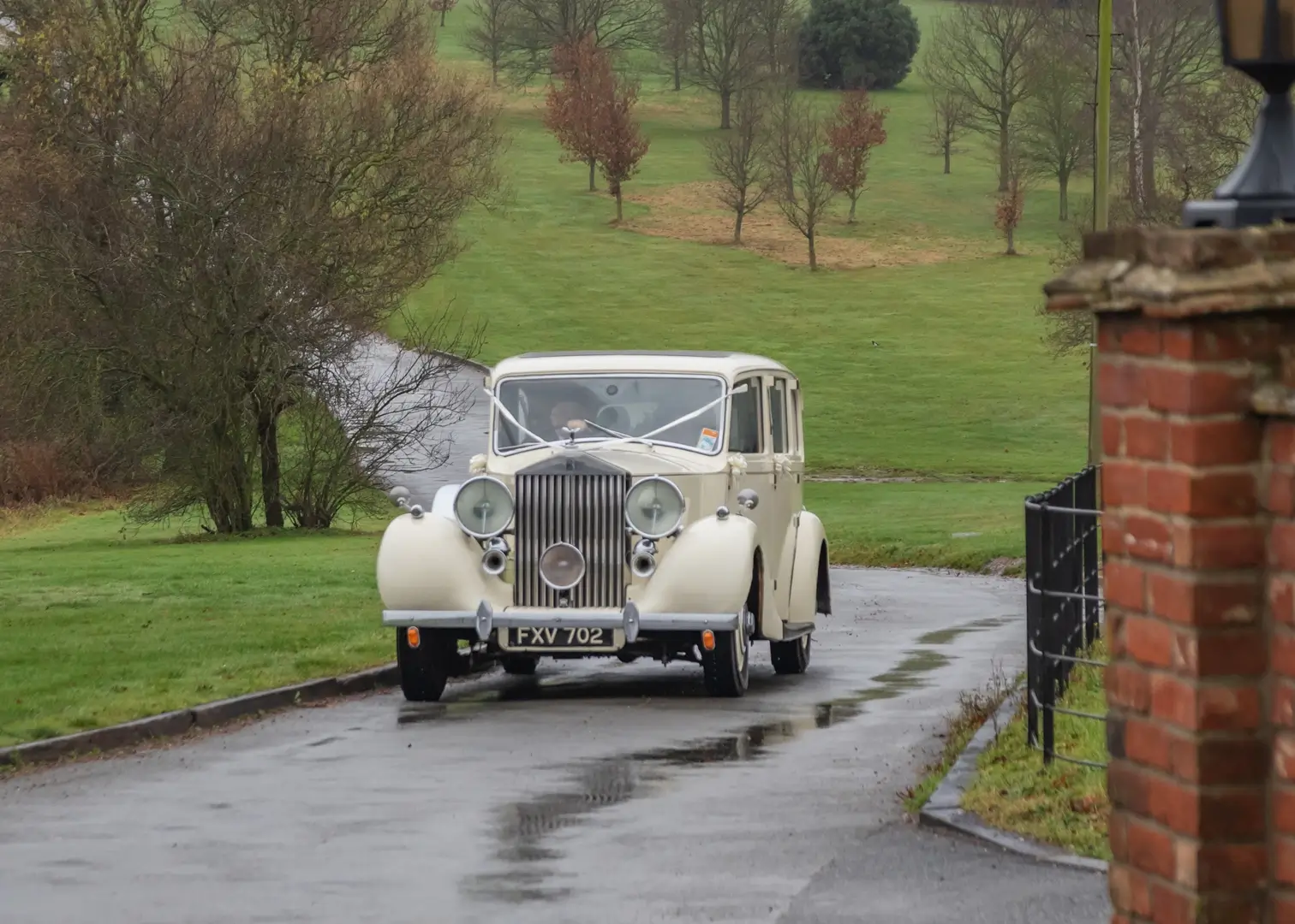 Vintage wedding car travels up the driveway in the rain at Crondon Park