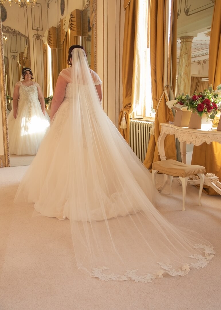 Bride gazing at her reflection in one of the mirrors in the gold coloured Rococco Suite at Gosfield Hall