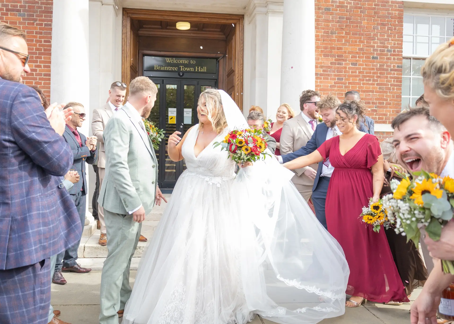 Wedding guests and couple laughing  after someone treads on the brides veil during the confetti at Braintree Town Hall