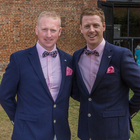 The groom and his best man in pink shirts and navy suit jackets with bow ties and pink pocket squares