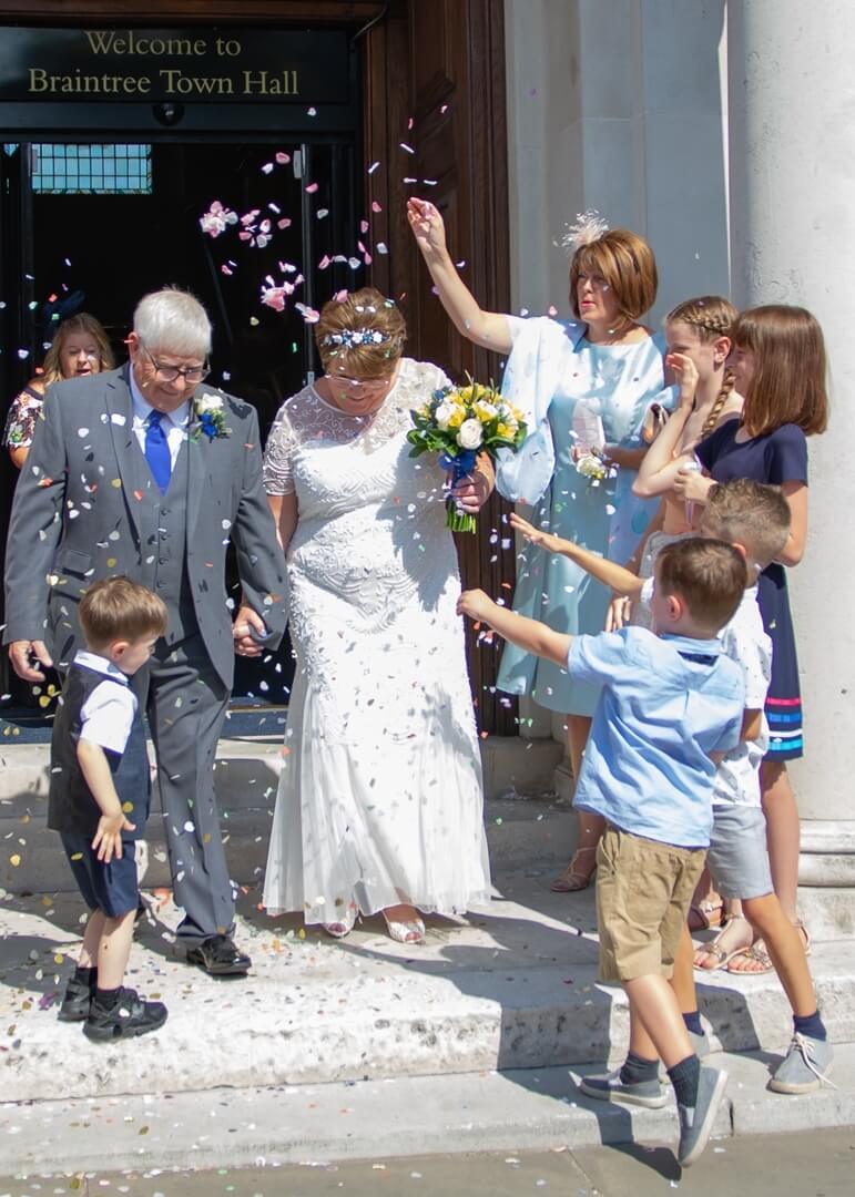 Bride and groom leaving Braintree Town Hall as guests throw confetti