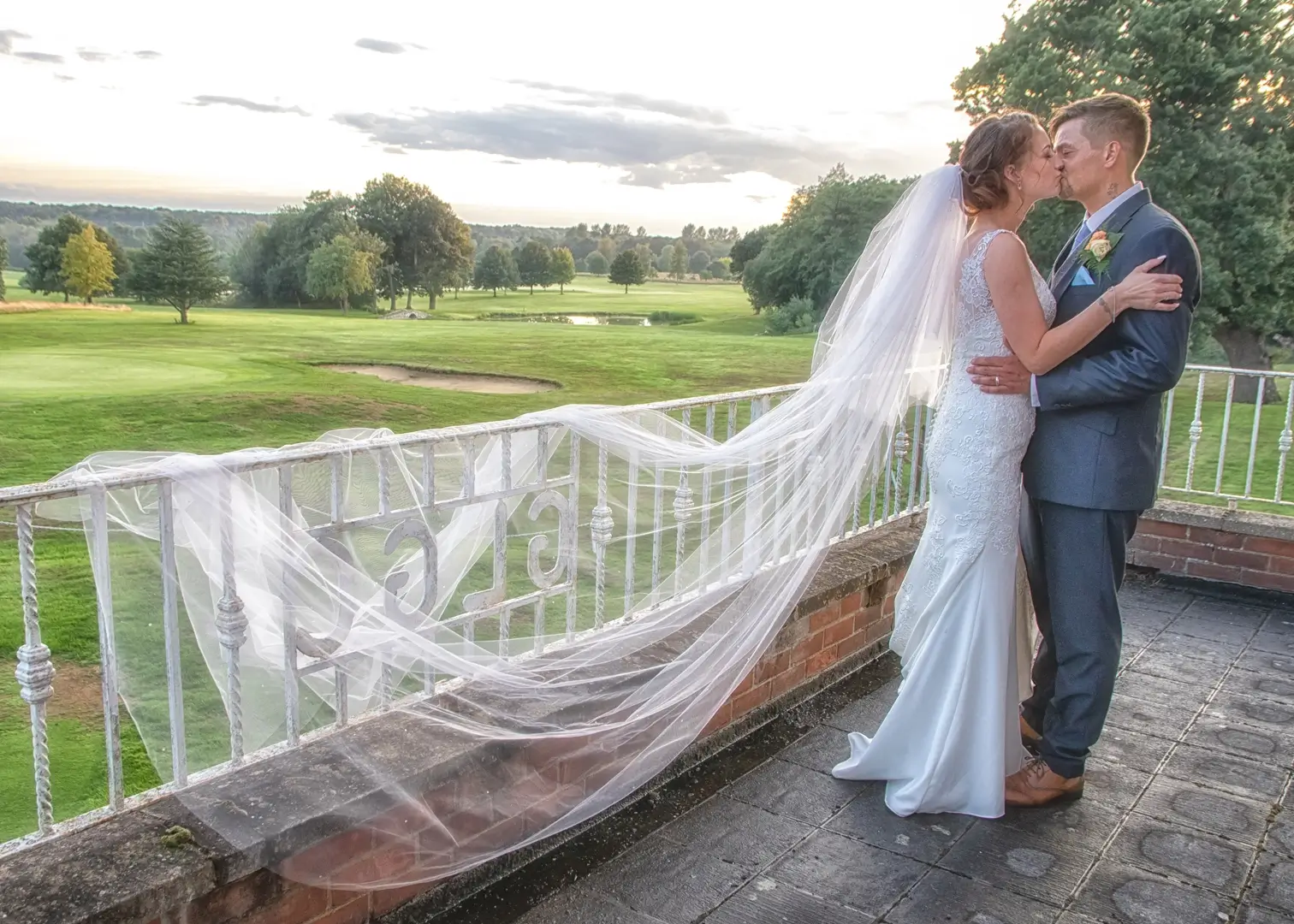 Bride and groom kiss on the balcony at Gosfield Lake Golf Club at sunset