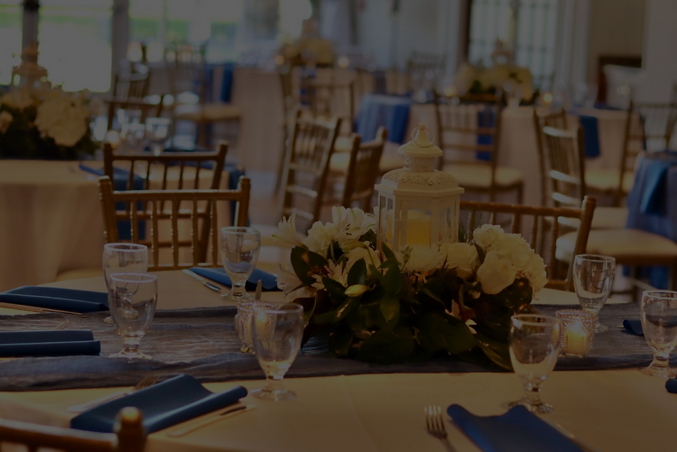 A wedding reception space is decorated with blue table settings and white centerpieces with greenery