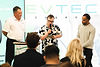 Three men at an event, one speaking into a microphone