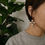 Thumbnail: Woman wearing Mye1038 - Fan Shape Drop Hoop Earrings, against a green background.