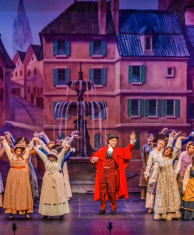 Scott is in period dress and a red coat among a crowd of chorus members.