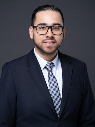 Headshot of a political candidate wearing a navy blue blazer, tie and white shirt