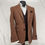 Thumbnail: A brown herringbone tweed blazer with dark brown trim on the pockets, worn over a dark brown waistcoat and white dress shirt.