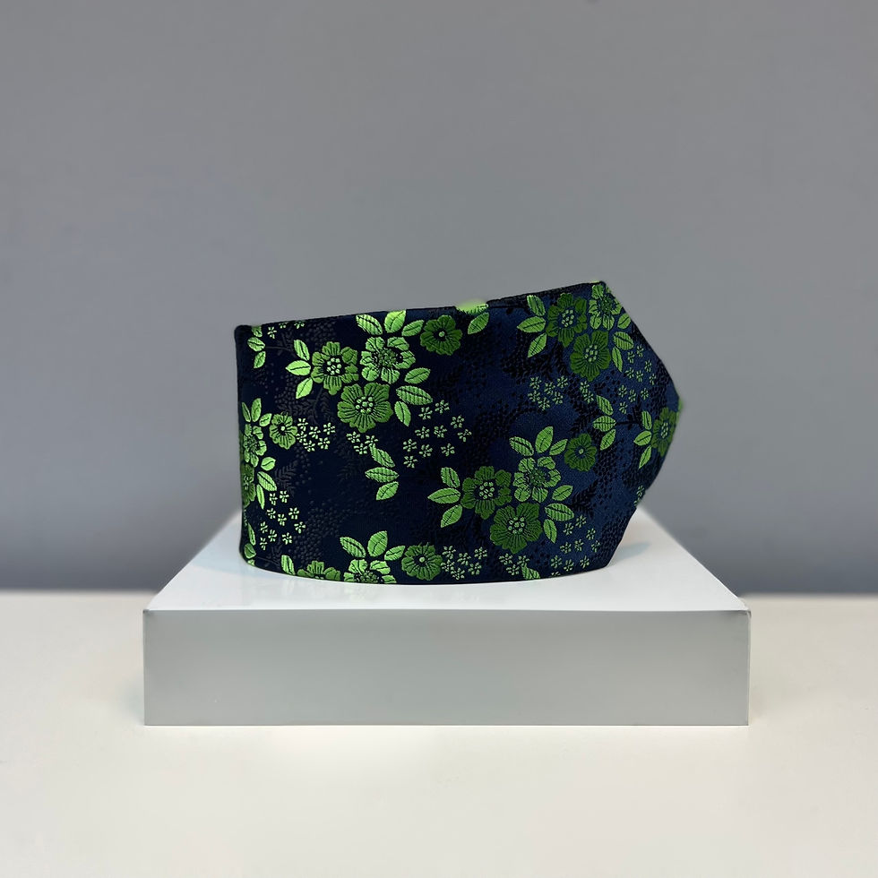 A navy silk tie showcasing a bright green floral pattern, neatly displayed on a white platform.