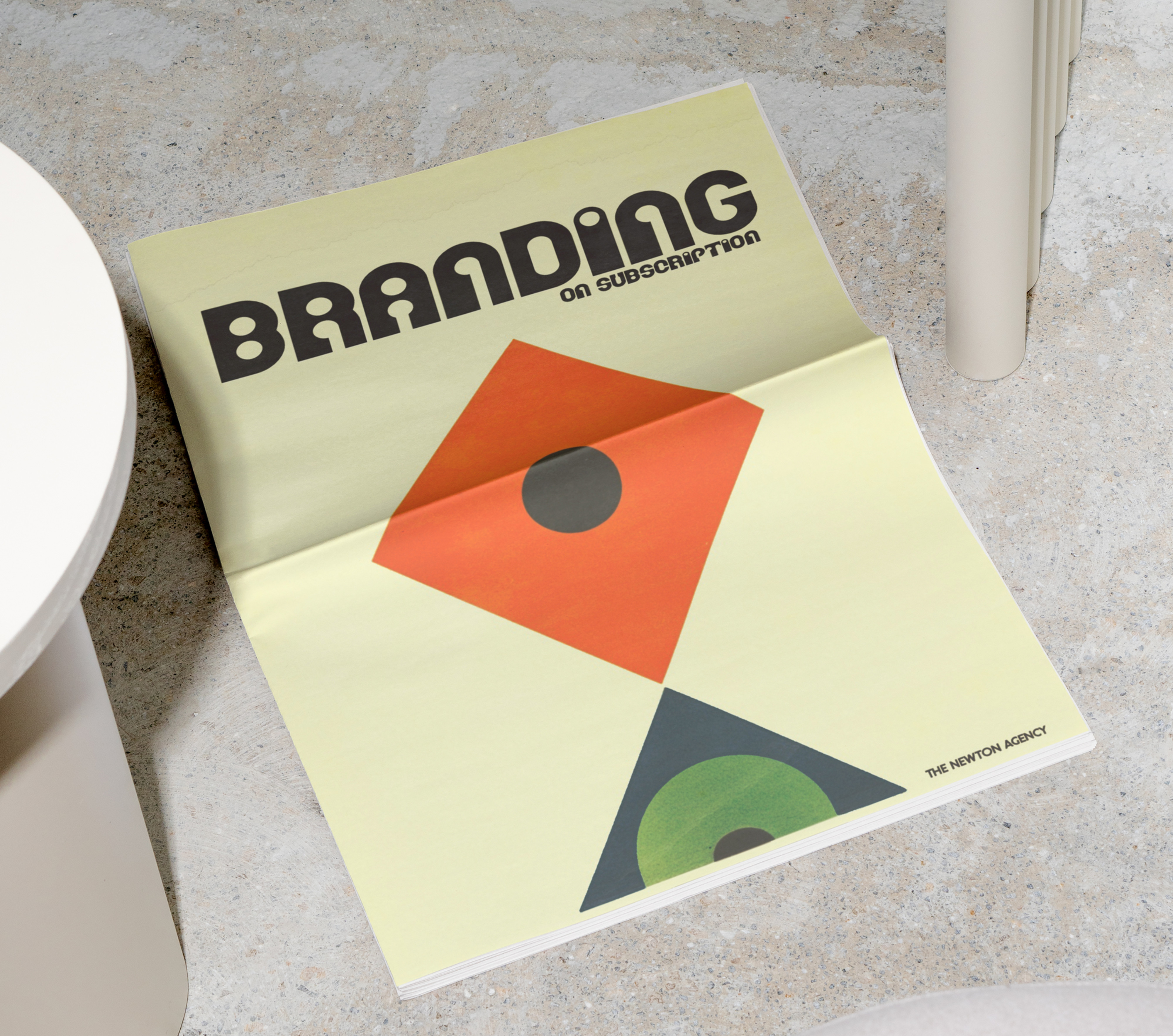 Magazine on a stone floor beside white chair legs, cover reading BRANDING on subscription with bold geometric shapes and a calm, minimalist look