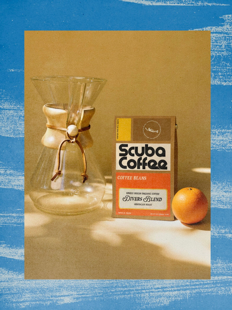 A glass coffee maker, Scuba Coffee package, and an orange rest on a beige surface with warm lighting. Blue border surrounds the image. Showing brand consistency by The Newton Agency