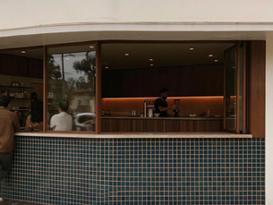 People wait at a modern coffee kiosk while a barista makes a drink inside, with blue tiled front and warm lighting.