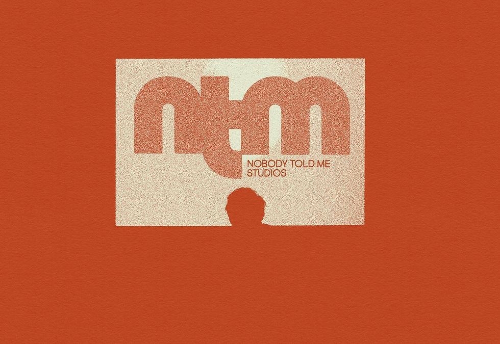 Orange poster with speckled white square, large n.m, and NOBODY TOLD ME STUDIOS text above a head silhouette.