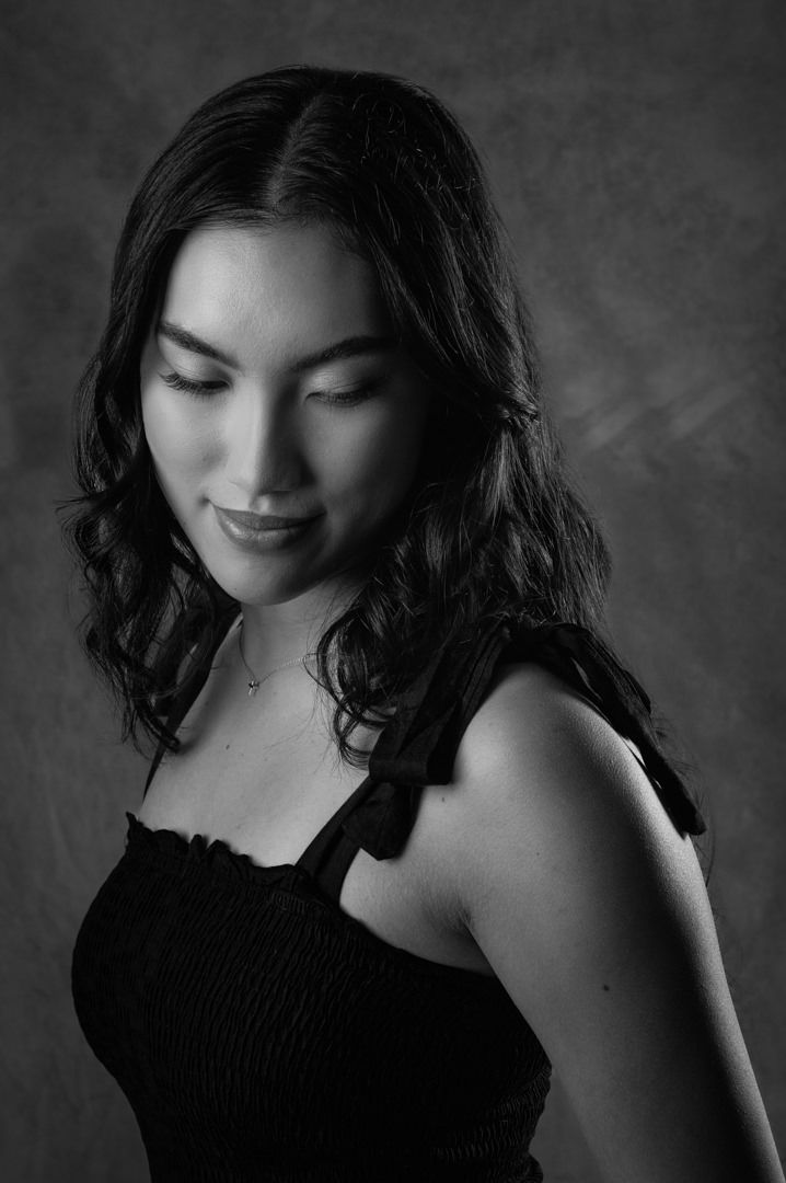 Black and white images of a Young woman wearing a black dress looking down at her shoulder