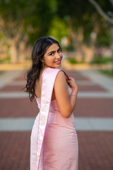 A woman wearing a pink dress and holding a pink stole over her shoulder looking back at the camera.