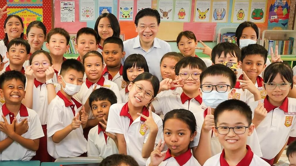 A group of smiling students in white and red uniforms pose in a colorful classroom. Posters and books line the background.
