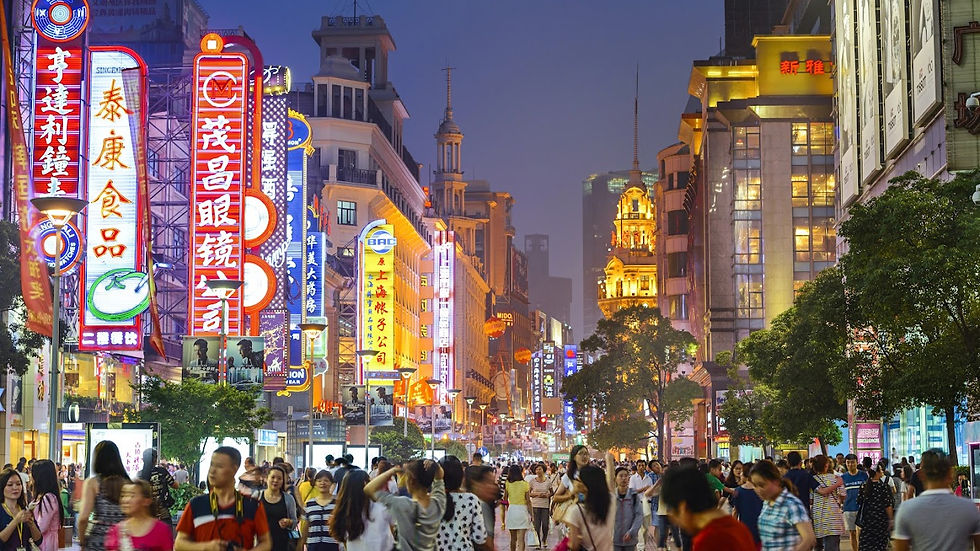 A bustling night scene on a vibrant city street lined with colorful neon signs and crowds of people walking past shops and lit buildings.