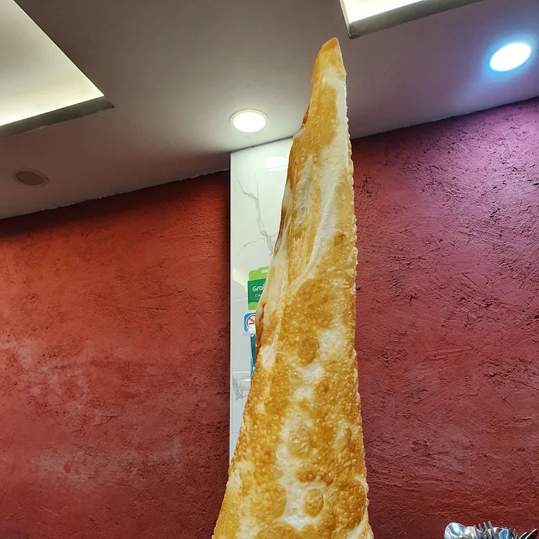 Tall cone-shaped fried bread on a green plate in a restaurant, with red walls and a utensil holder on the table.