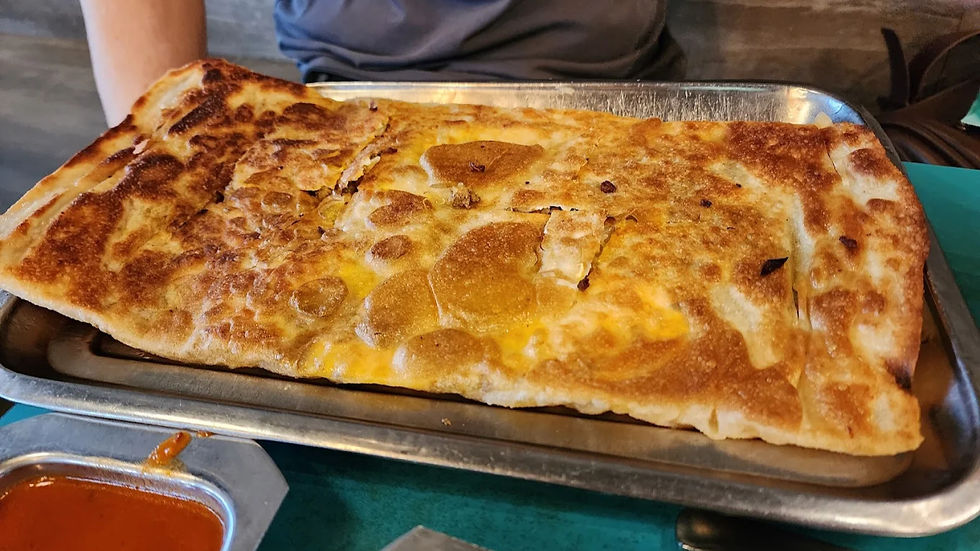 Crispy Roti Prata on a metal tray with spicy dipping sauce. Background shows part of a person's torso in casual attire. Warm, appetizing mood.