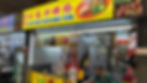 Food stall with a bright yellow sign reads "Day Night Fried Kway Teow." A vendor in a green shirt is cooking. The stall has various food awards displayed.