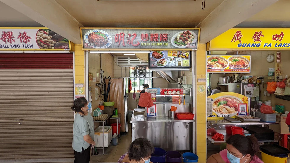 Hawker stall setting with people wearing masks. Signs read "MENG KEE FRIED KWAY TEOW" and "GUANG FA LAKSA." Bright, busy atmosphere.