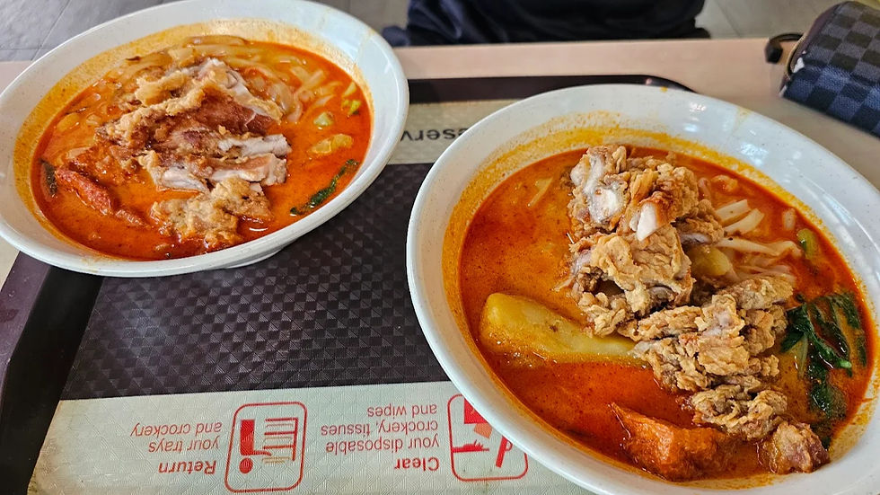 Two bowls of curry noodles with fried chicken on a tray. The rich orange broth contrasts with the white bowls. A placemat with care instructions is visible.
