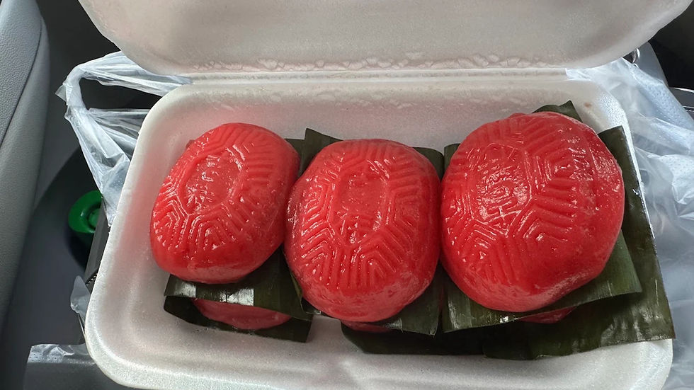 Three red patterned steamed cakes on banana leaves in an open foam takeout box inside a car.