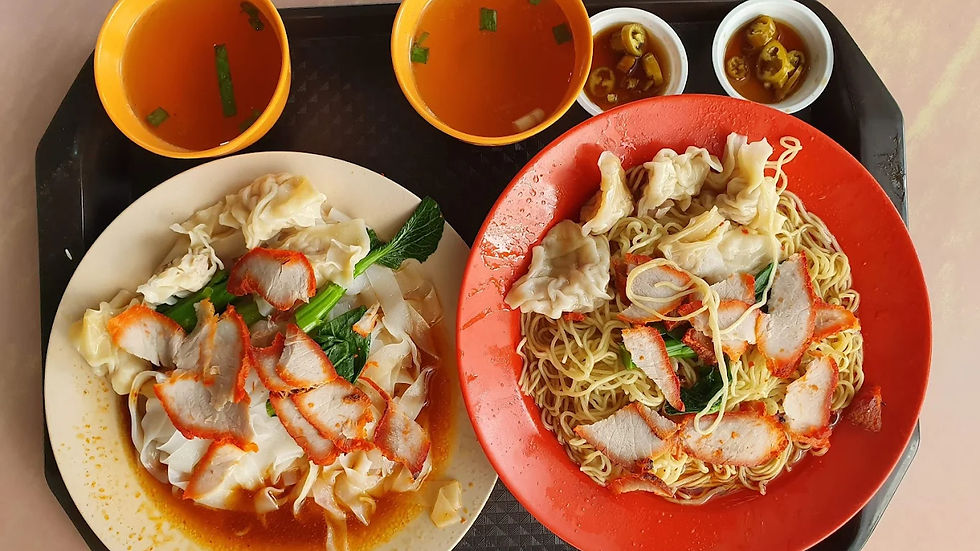 Two plates of noodle dishes with sliced pork and dumplings on colorful round plates, accompanied by two bowls of soup and condiments.