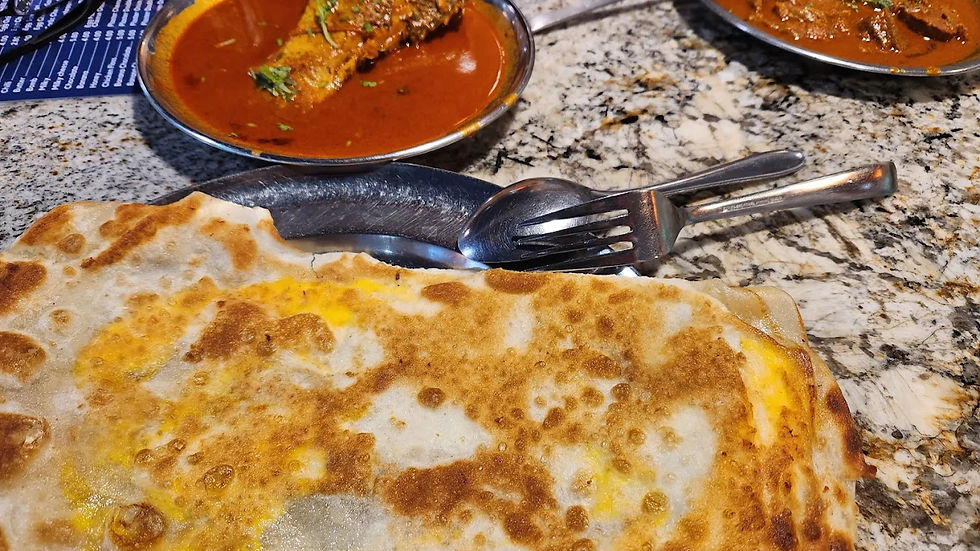 Egg-stuffed paratha on a granite table, with metal cutlery and plates of spicy curry nearby, creating a warm, appetizing scene.