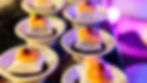 Small plates with gourmet appetizers, featuring salmon and garnish, arranged neatly on a reflective surface. Purple ambient lighting.