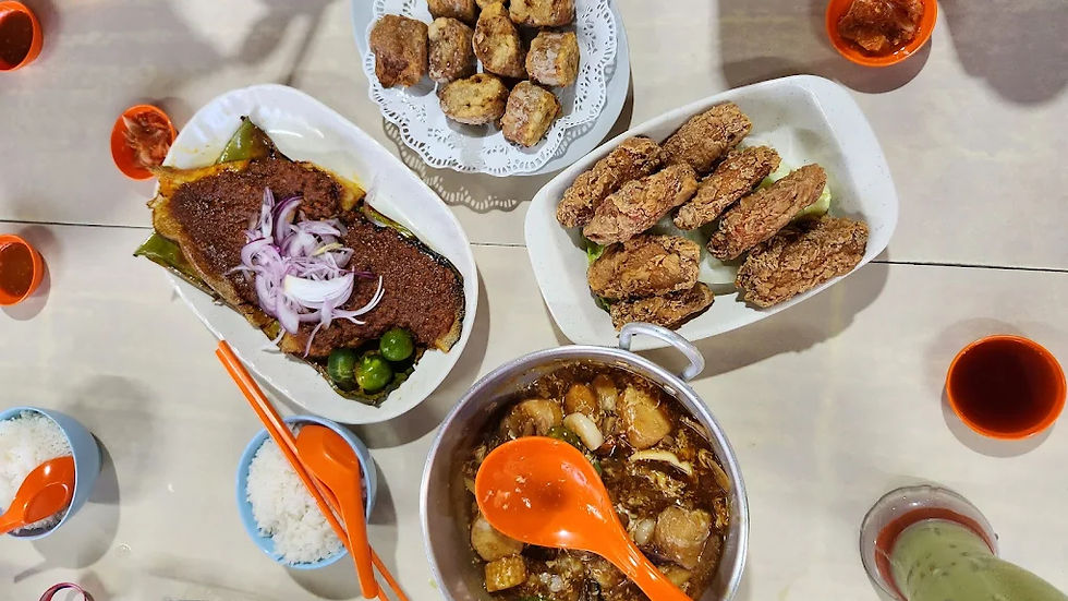 Assorted dishes on a table include a fish topped with onions, fried items, soup with a ladle, and rice. Red and blue bowls add color.