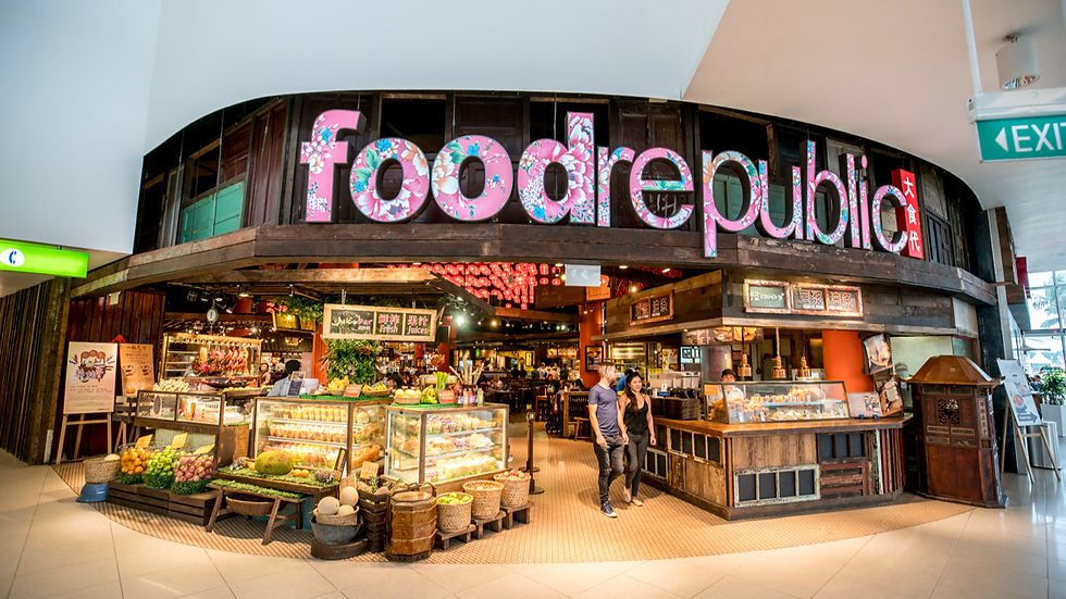 A couple walks past a vibrant "food republic" sign adorned with floral patterns, outside a bustling indoor food market with colorful displays.