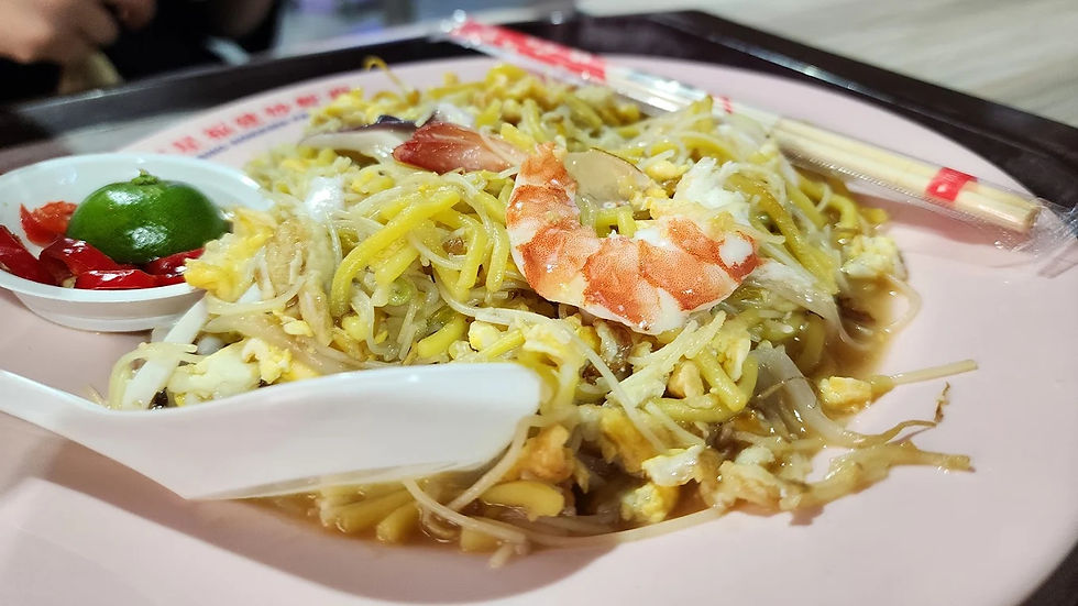 A plate of fried noodles topped with shrimp, bean sprouts, and egg. Garnished with lime and red chili on the side. Chopsticks nearby.