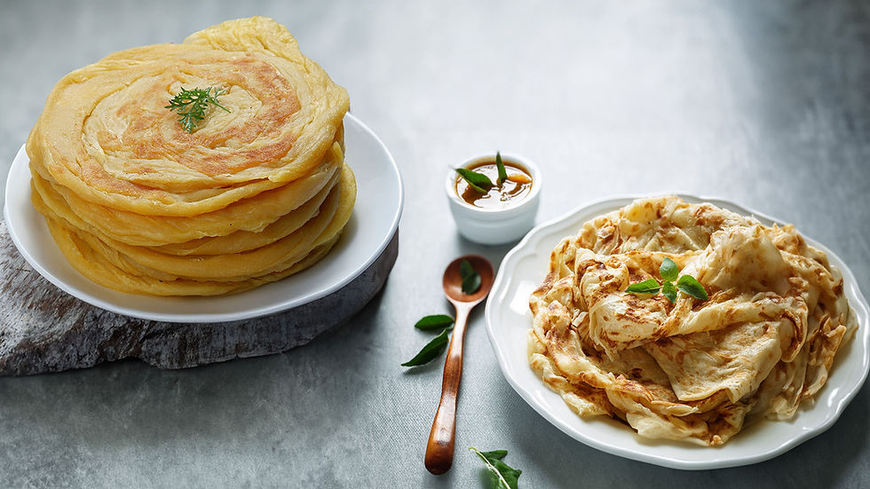 Two plates of Indian flatbreads on a gray surface. One plate has a stack of plain parathas with garnish, the other has folded parathas.