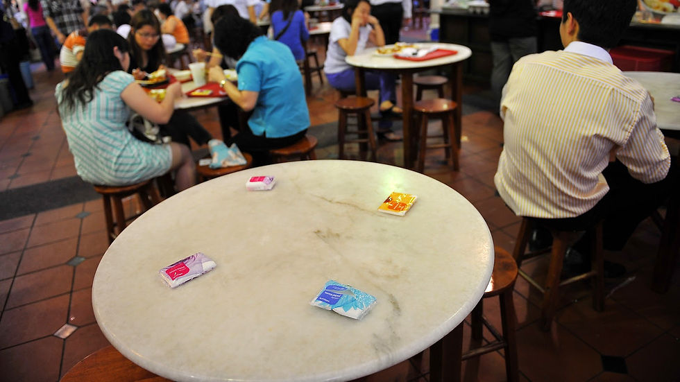 Empty marble table with tissue packets in a busy food court. People dining at surrounding tables. Warm lighting, casual atmosphere.